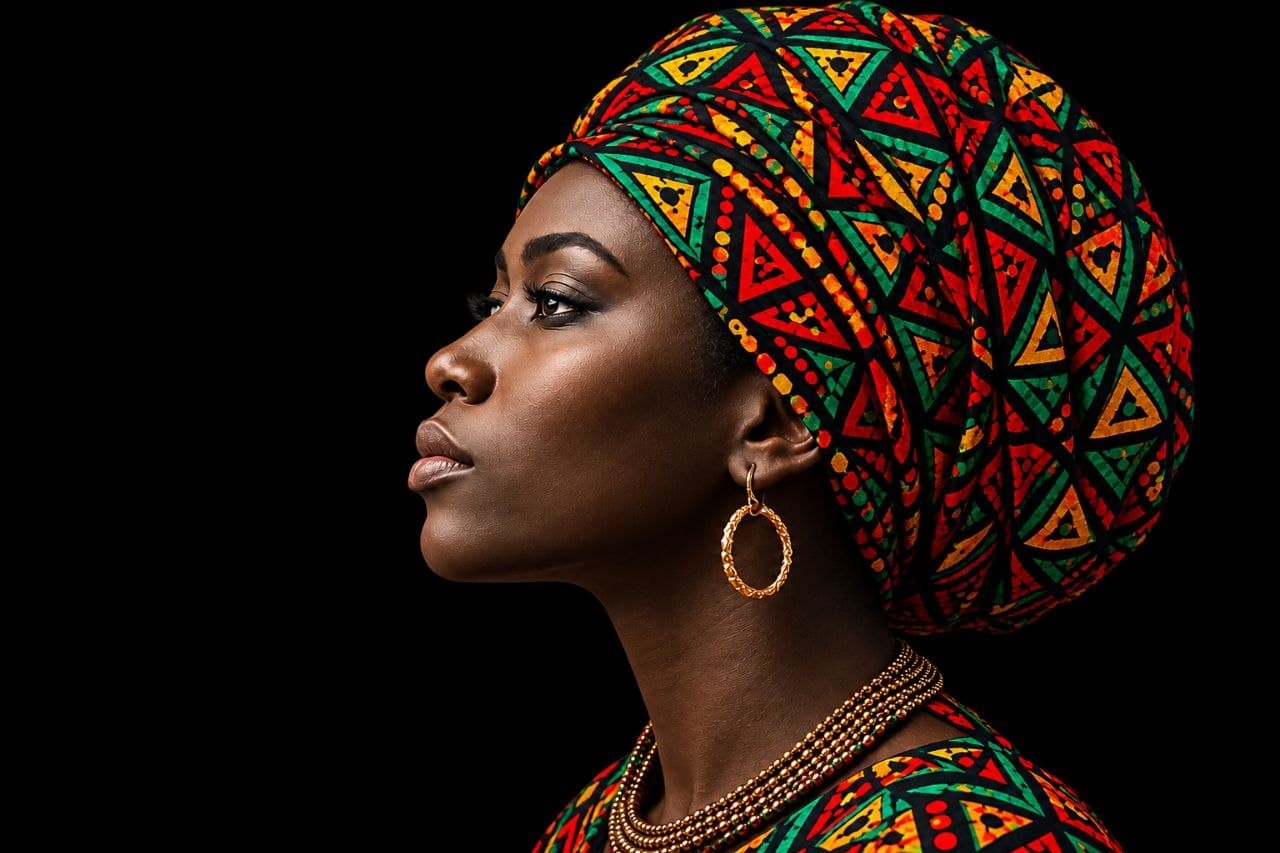 Side profile of a woman wearing a colorful tribal-print headwrap and gold jewelry